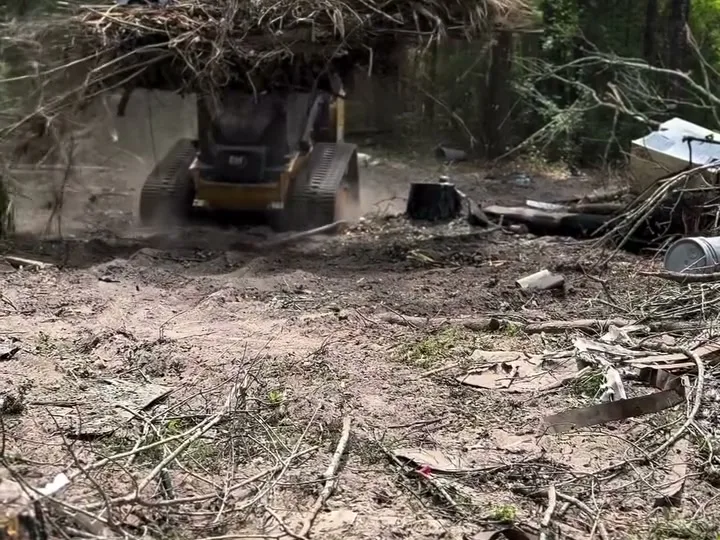 Track loader carrying a full grapple of brush across a yard