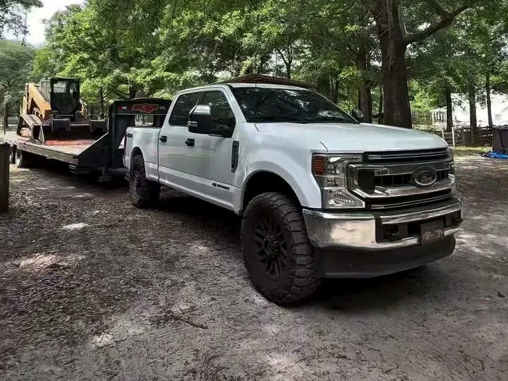 Pickup and gooseneck trailer staged under the oaks with a machine