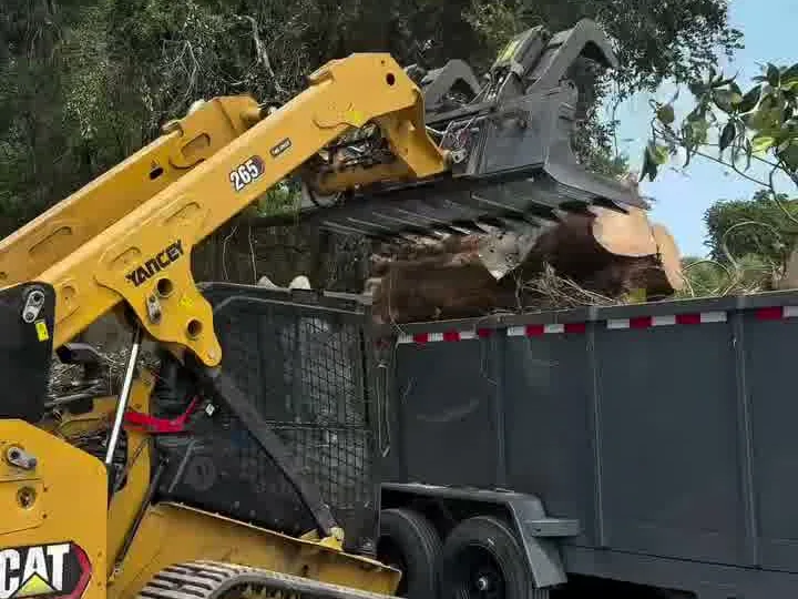Skid steer services: track loader grapple loading a log onto a dump trailer